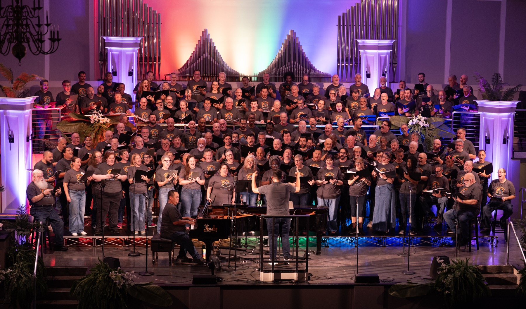 Florida GALA choruses performing together on stage under rainbow lighting.